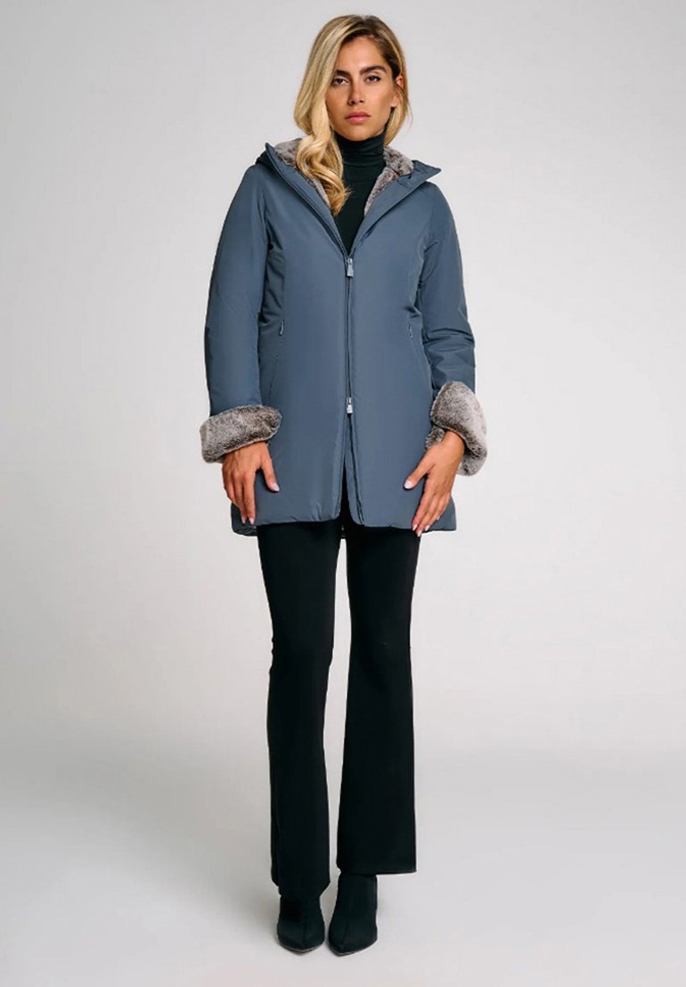 Cappotto grigio isolato con colletto e polsini in pelliccia sintetica, cappuccio, chiusura frontale con zip e due tasche laterali, abbinato a pantaloni neri aderenti.