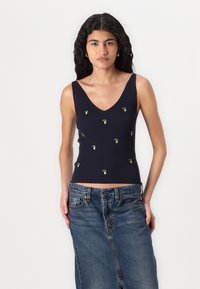 Temno modra rebrasta majica brez rokavov z globokim V-izrezom in drobnimi zelenimi vezenimi listi. V kombinaciji z svetlo modrim jeans krilom.