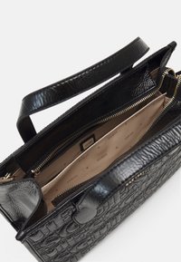 Černá kabelka s texturovaným, reliéfním povrchem. Obsahuje kapsy na zip a béžovou vnitřní podšívku s jemným vzorem značky.