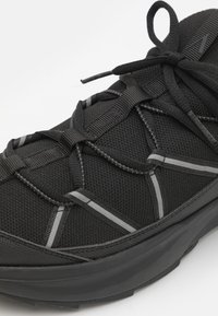 Baskets noires en tissu mesh respirant, avec une surface texturée, un système de laçage structuré et des accents gris contrastants.