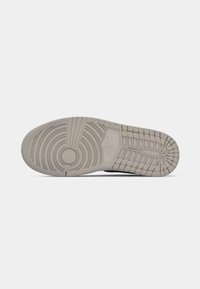 Suola di scarpa con un design testurizzato di colore grigio chiaro, caratterizzata da scanalature circolari e orizzontali. Logo del marchio impresso vicino al centro.