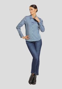 Hellblaues Hemd mit Kragen, langen Ärmeln und glatter Textur, kombiniert mit dunklen Skinny Jeans und schwarzen Stiefeletten.