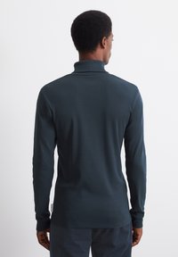 Marineblauwe polo met lange mouwen en hoge kraag, gemaakt van een gladde stof. Heeft aansluitende mouwen en een zijlabel nabij de zoom.