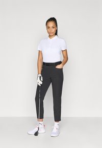 Λευκό πόλο πουκάμισο, μαύρο ραμμένο παντελόνι, λευκά αθλητικά παπούτσια με ροζ λεπτομέρειες, κρατώντας μπαστούνι γκολφ, φορώντας γάντι γκολφ.