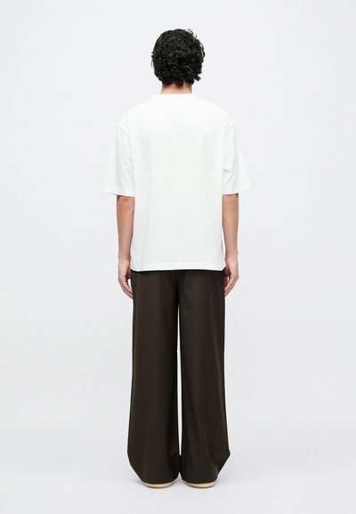 Tricou alb cu mâneci scurte, croială lejeră, asortat cu pantaloni largi de culoare maro închis. Textură fină, asemănătoare bumbacului, design minimalist.