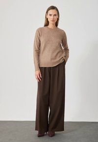 Μπεζ πλεκτό πουλόβερ με στρογγυλή λαιμόκοψη και ριμπ τελείωμα, συνδυασμένο με παντελόνι καφέ φαρδιάς γραμμής. Λεπτή υφή, μινιμαλιστικός σχεδιασμός.