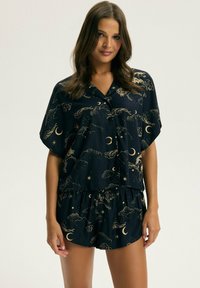 Granatowy zestaw piżamowy z krótkim rękawem i szortami, zdobiony złotymi niebiańskimi wzorami księżyców, gwiazd i mitycznych stworzeń. Miękka tkanina.