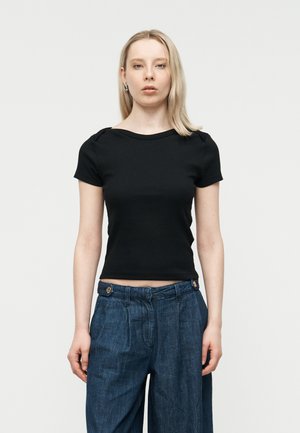 Young woman with blonde hair wearing a black fitted short-sleeve top and high-waisted blue wide-leg jeans against a plain background.