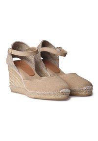 Beige espadrilky na klínovém podpatku s textilním svrškem, nastavovacím páskem kolem kotníku a jutu jako podešví. Vyznačují se hladkým povrchem a zaoblenou špičkou se šitými detaily.