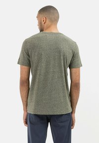 T-shirt z krótkim rękawem i okrągłym dekoltem w melanżowym zielonym materiale, z teksturowanym wykończeniem, noszony z granatowymi spodniami, widok z tyłu.
