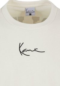 Vit bomull t-shirt med korta ärmar, ribbad rund halsringning och svart broderad logotyp på bröstet. Storleksmärkning "L" synlig.
