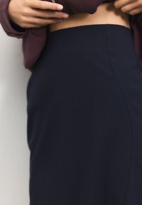 Jupe crayon bleu marine en tissu lisse, avec une silhouette ajustée et une taille sans coutures, présentée avec un haut bordeaux.