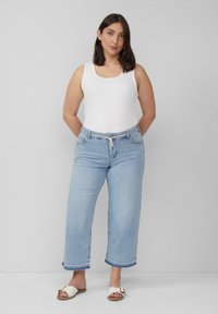 Lichtblauwe denim wijde broek met een onbewerkte zoom, gecombineerd met een witte tanktop en witte sandalen, met een koord in de taille.