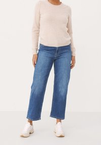 Jasnoróżowy sweter z długim rękawem w połączeniu z niebieskimi dżinsami o średnim stanie i szerokich nogawkach oraz białymi sneakersami. Miękka tekstura; prosty wzór; brak wzorów.