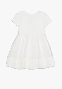 Weißes Kleid mit kurzen Ärmeln, aus floralem Spitze mit einer Netzunterlage. Rundhalsausschnitt und schmeichelnder Rock mit strukturiertem Blumenmuster.