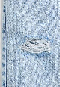 Helles blaues Denim-Gewebe mit einem beschädigten Bereich und ausgefransten Kanten. Die Gesamttextur ist glatt mit einem dezenten abgenutzten Aussehen.