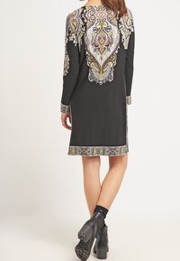 Robe noire à manches longues ornée d'une broderie cachemire multicolore complexe au dos et à l'ourlet, associée à des bottes noires épaisses.