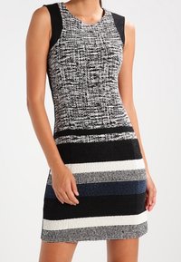 Robe sans manches avec un haut texturé noir et blanc, présentant des rayures horizontales noires, bleues et blanches sur la jupe. Fabriquée en tissu tissé.