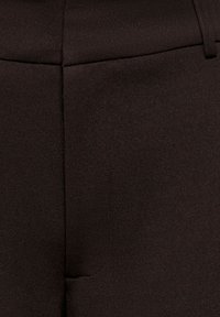 Κοντινό πλάνο σκούρου καφέ υφάσματος με κάθετες ραφές και θηλιά ζώνης στην επάνω δεξιά γωνία.