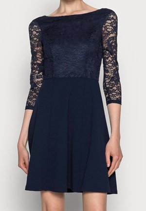 Marineblaues Kleid mit Spitzenoberteil und dreiviertel Ärmeln, ausgestelltem Rock, glatter Textur und Bootsausschnitt.