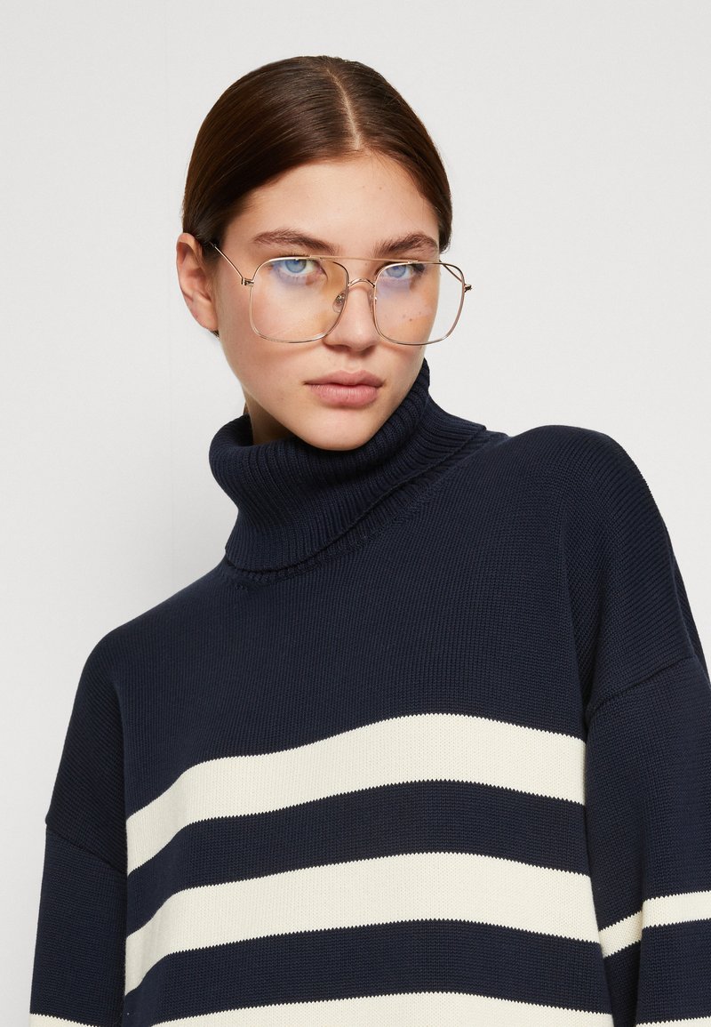 Granatowy sweter z golfem wykonany z dzianiny, z białymi poziomymi paskami. Posiada teksturowany materiał i luźny krój, zaprojektowany z wysokim dekoltem.