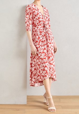 Robe florale rouge avec des motifs de feuilles blanches, dotée d'un décolleté en V, de manches courtes et d'une silhouette fluide arrivant au genou avec une taille froncée.