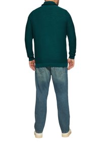 Donkerblauwe lange mouwen polo met een geribbelde textuur, gekenmerkt door een opgerolde kraag, gecombineerd met vervaagde blauwe jeans en crèmekleurige sneakers.