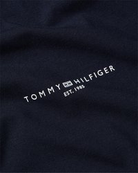 Logo Tommy Hilfiger se symbolem vlajky a nápisem "EST. 1985" tištěným bílou barvou na tmavě modré tkanině.