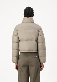 Kuttet, lys beige pufferjakke med høy krage og kviltet design. Kombinert med olivengrønne cargo-bukser med sidelommer.