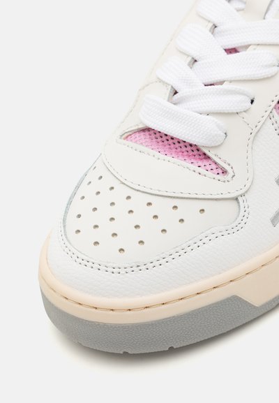 White leather sneaker with pink mesh accents, perforated toe, white laces, and a textured gray rubber sole. Rounded shape and modern design.