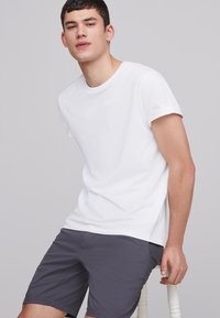 T-shirt en coton blanc avec col rond et manches courtes retroussées, associé à un short gris. Texture lisse, coupe décontractée et design simple.