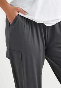 Grijze broek van zachte stof met een elastische tailleband, zijzakken en een cargozak op het linkerpand.