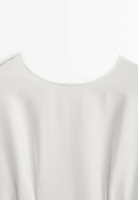 Vêtement blanc avec un large col rond, une texture lisse et un design fluide. Le tissu tombe doucement, présentant de légers plis sur les côtés.