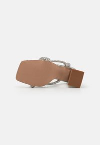 Sandalo con tacco argento, caratterizzato da cinturini incrociati adornati con strass. Presenta un tacco quadrato e una suola beige texturizzata.