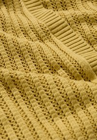 Gelbes gestricktes Material mit einer strukturierten Musterung, die abwechselnd Abschnitte mit offener Webart und Rippstrick aufweist, was einen dynamischen visuellen Effekt erzeugt.