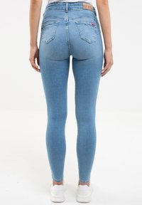 Jeans ajustados de color azul claro con una cintura alta, que cuentan con bolsillos traseros y un acabado de denim texturizado. Combinados con zapatillas blancas.