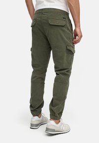Pantaloni cargo verde oliva con polsini affusolati, diverse tasche e tessuto morbido. Indossati con sneakers atletiche grigie e bianche.