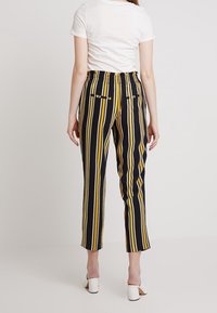 Svarta och gula randiga byxor med elastisk midja, kort design och två bakfickor. Matchade med vita klackar.