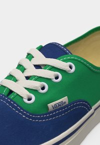 Baskets Vans basses avec toile verte, accents en suède bleu, lacets blancs et semelle en caoutchouc blanche.