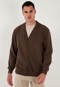 Cardigan marrone realizzato in morbido tessuto a maglia, con scollo a V, chiusura con bottoni, polsini a costine e un fit rilassato. Texture liscia e design semplice.