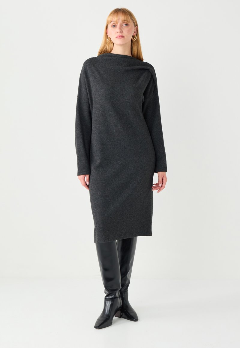 Robe à manches longues gris charbon avec un col bénitier, présentant une coupe ajustée et une longueur mi-mollet. Associée à des bottes noires montantes jusqu'aux genoux.