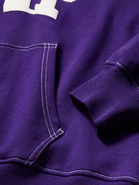 Tissu de sweat-shirt violet avec coutures blanches visibles, poche avant et détail de poignets en côte.