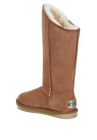 Botte haute en suède beige avec une douce doublure en fourrure blanche, bout arrondi et semelle en caoutchouc. Présente une étiquette métallique sur le côté extérieur.