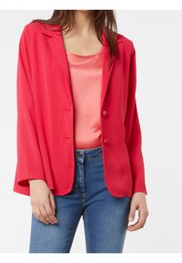Blazer rouge à coupe décontractée, avec deux boutons et des revers arrondis, associé à un débardeur rose clair et un jean bleu. Texture de tissu lisse.