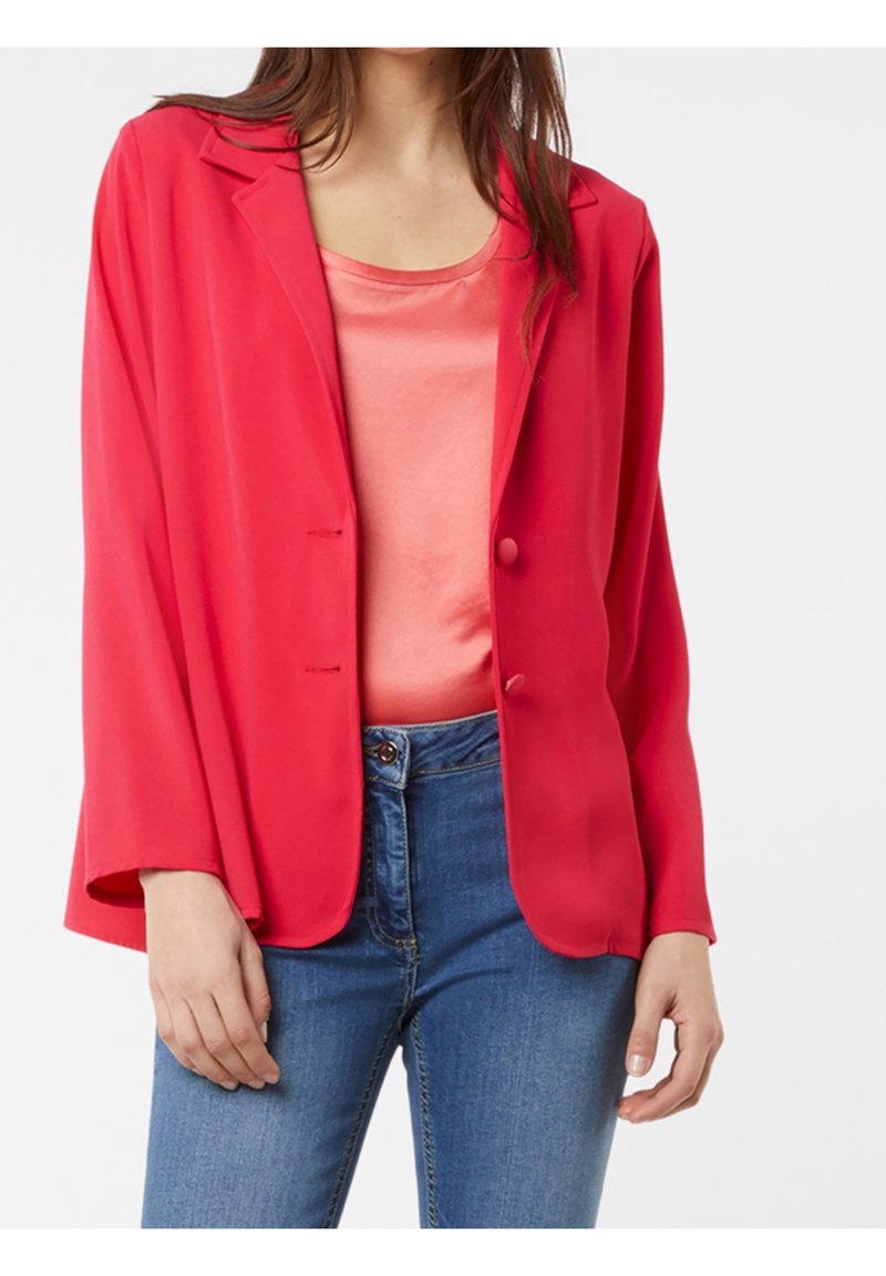 Blazer rouge à coupe décontractée, avec deux boutons et des revers arrondis, associé à un débardeur rose clair et un jean bleu. Texture de tissu lisse.