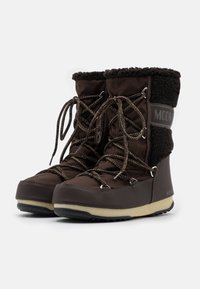 Bottes isolées marron avec bord en fausse fourrure, design à lacets, semelle en caoutchouc et bout renforcé. Marque visible sur le côté.