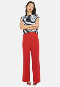 Punased laiad püksid, millel on vormitud vöökoht, koos mereväe- ja valge triibulise lühikese varrukaga topiga. Hõbedased kingad, minimalistlik disain.