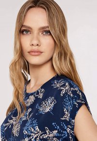 Marinebluse mit kurzen Ärmeln, versehen mit einem Muster aus blauen und beigen Blumen. Glattes Material und runder Ausschnitt.