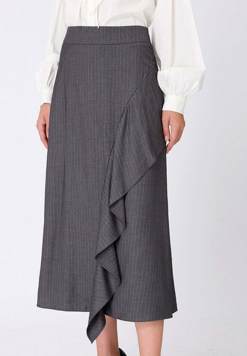 Jupe grise à rayures avec un ourlet froncé, présentant une texture lisse et un design taille haute, associée à un chemisier blanc.