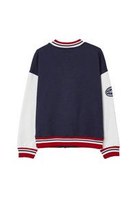 Marineblaue Collegejacke mit weißen Ärmeln, rotem und weißem gestreiften Bündchen und Saum sowie einem Aufnäher am rechten Ärmel.